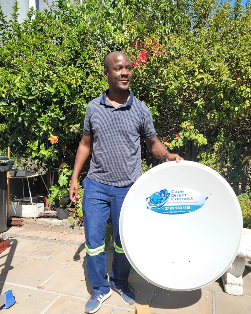 Technician holding a satellite dish beside a service vehicle